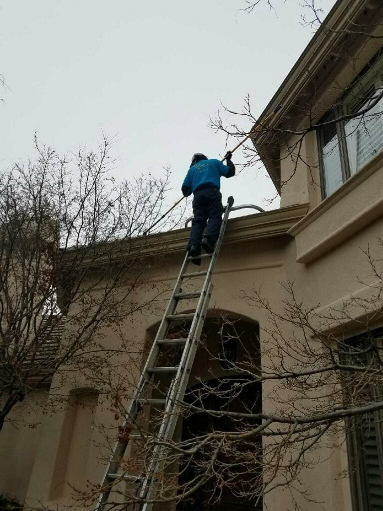 Technician on a ladder removing debris from the roofline of a second-story home